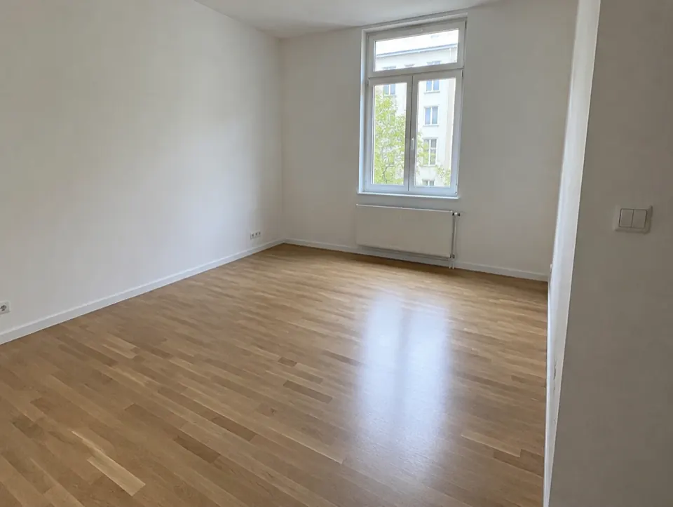 Empty living room at move-in with clean walls and an unmarked oak floor